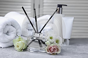 Towels, reed air freshener, cosmetic products and flowers on grey table indoors