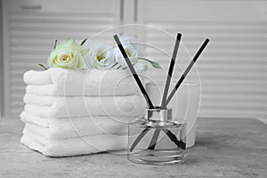 Towels, reed air freshener, scented candle and flowers on grey table indoors