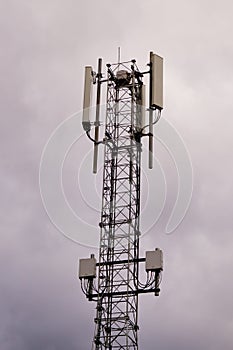 Tower with 5G and 4G cellular network antenna on grey cloudy sky background