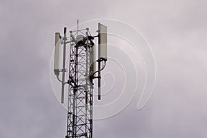 Tower with 5G and 4G cellular network antenna on grey cloudy sky background