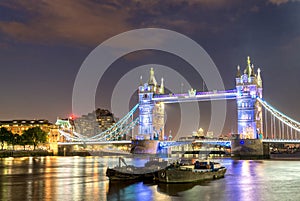 The Tower Bridge at night with boats on Thames river - London -