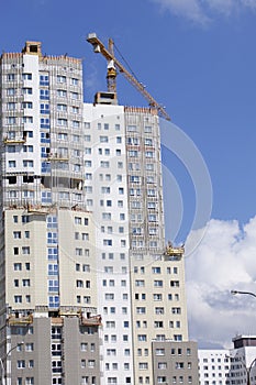 Tower building crane against the blue sky. On the wall of the building are hung winches for exterior decoration. The buildings und