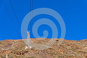 The tower of the cable car on the background of the volcano and the blue sky