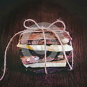 A tower of chocolate bars wrapped like a chocolate present . Various chocolate pieces over dark wood background.