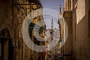 The tower of the christian church is seen through the narrow street alley in Old Town of Jerusalem.