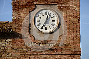 Tower clock with Roman numerals in front of brick wall