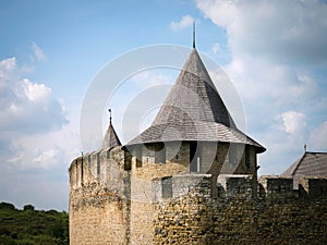 Tower with a conical roof and merlons of a medieval castle against a blue sky