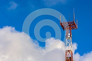 Tower connection with the mast and antennas against the blue sky with clouds. Transmission and reception of signals.