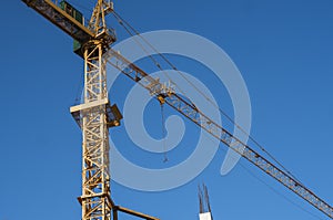 Tower crane against blue sky on a construction site for building of multi storage building or another type of structure.