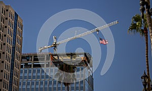 Tower Crane with an American flag near a modern office building under construction against a blue sky