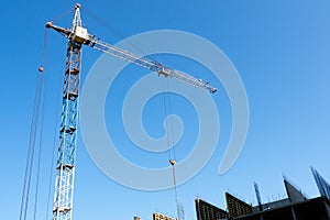 Tower crane on the background of the blue sky in the lower part of the picture part of the building under construction