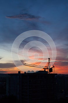 Tower crane and building construction site silhouette at sunrise.