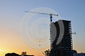 Tower crane constructing a new residential building at a construction site at sunset background.