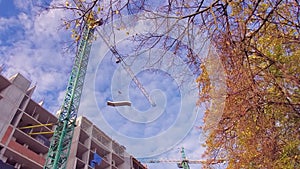 Tower Crane on a Construction Site Lifts a Load at High-rise Building on a background of blue autumn sky. Building Under Construct