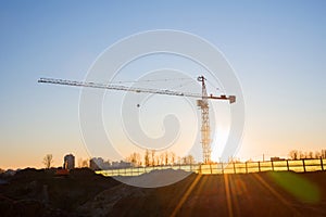 Tower crane at construction site on sunset background. Construction crane constructing a new residential building.