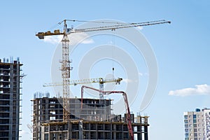 Tower crane lifting a concrete bucket at construction site. Workers during formworks and pouring concrete through a Ñoncrete pump