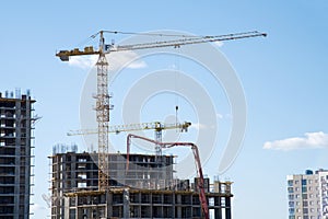 Tower crane lifting a concrete bucket at construction site. Workers during formworks and pouring concrete through a ÃÂoncrete pump photo
