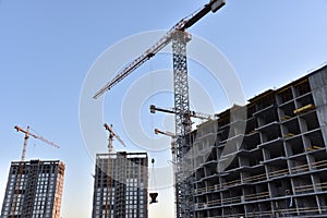 Tower crane lifting concrete bucket for pouring concrete during construction new residential building on blue sky background.