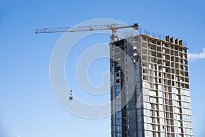 Tower crane lifting concrete bucket for pouring concrete during construction new residential building on blue sky background.