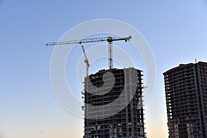 Tower crane lifting concrete bucket for pouring concrete during construction new residential building on blue sky background.