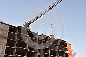 Tower crane lifting concrete bucket for pouring concrete during construction new residential building on blue sky background.