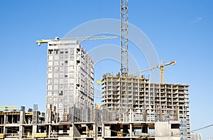 Tower crane lifting concrete bucket for pouring concrete during construction new residential building on blue sky background.