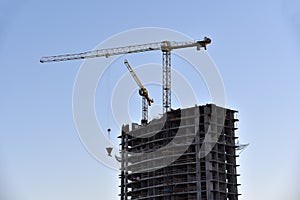 Tower crane lifting concrete bucket for pouring concrete during construction new residential building on blue sky background.