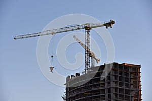 Tower crane lifting concrete bucket for pouring concrete during construction new residential building on blue sky background.