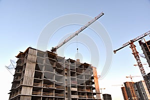 Tower crane lifting concrete bucket for pouring concrete during construction new residential building on blue sky background.