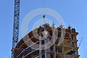 Tower crane lifting concrete bucket for pouring concrete during construction residential building on blue sky background. Builder
