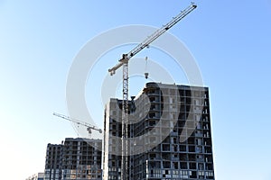 Tower crane lifting concrete bucket for pouring concrete during construction residential building on blue sky background. Builder