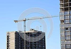 Tower crane lifting concrete bucket for pouring concrete during construction residential building on blue sky background. Builder