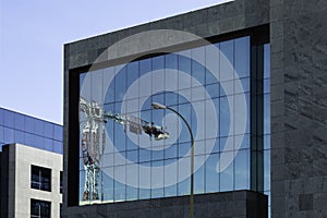 Tower crane reflected in the front of an office building