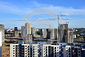 Tower cranes in action on blue sky background. Drone view on construction of new multi-storey buildings. Residential building is
