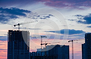 Tower cranes in action at construction site on sunset background. Crane the build the high-rise building. New residential