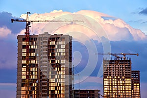 Tower cranes in action at construction site on sunset background. Crane the build the high-rise building. New residential