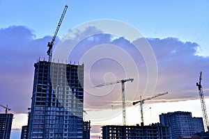 Tower cranes in action at construction site on sunset background. Crane the build the high-rise building. New residential