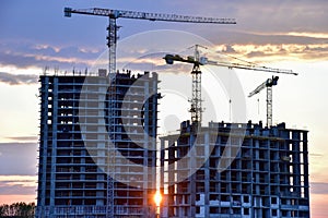 Tower cranes in action at construction site on sunset background. Crane the build the high-rise building. New residential