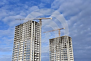 Tower cranes build the high-rise building. Crane working at construction site. New residential skyscraper on blue sky background