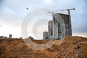 Tower cranes build the high-rise buildings. Crane working at construction site. New residential skyscraper on sunset background.