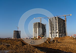 Tower cranes and building silhouette at construction site on  sunset background. Excavator digs the ground for the foundation and