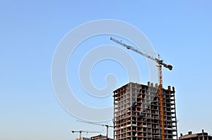 Tower cranes constructing a new building at a construction site on the sunset and blue sky background.