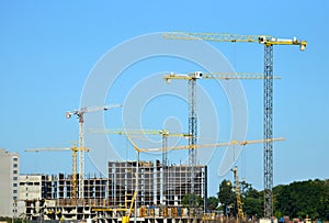 Tower cranes constructing a new residential building at a construction site against blue sky.