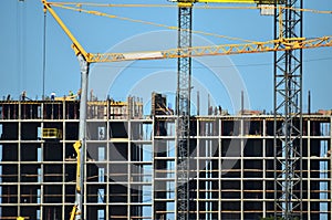 Tower cranes constructing a new residential building at a construction site against blue sky.