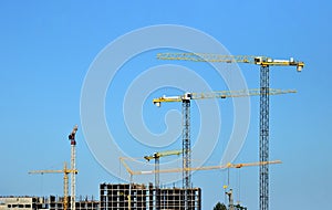 Tower cranes constructing a new residential building at a construction site against blue sky.