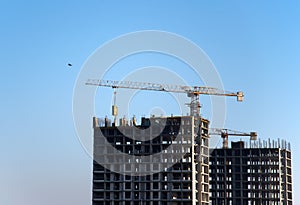 Tower cranes constructing a new residential building at a construction site against blue sky.