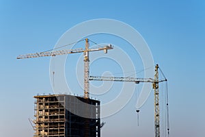 Tower cranes constructing a new residential building at a construction site against blue sky. Renovation program, development,