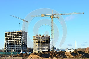 Tower cranes constructing a new residential building at a construction site against blue sky. Renovation program, development,