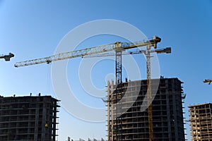 Tower cranes constructing a new residential building at a construction site against blue sky. Renovation program, development,