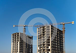 Tower cranes constructing a new residential building at a construction site against blue sky. Renovation program, development,